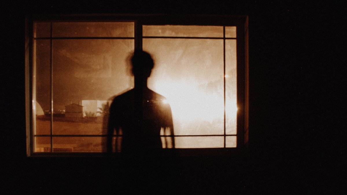 Person standing before window in dark room looking at bright light.